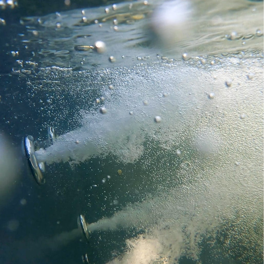 Unterwasseransicht von zwei Metall-Wasserdüsen, die Luftblasen in klares Wasser abgeben