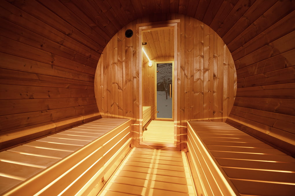 Wooden sauna interior with benches and lighting with a door leading outside.