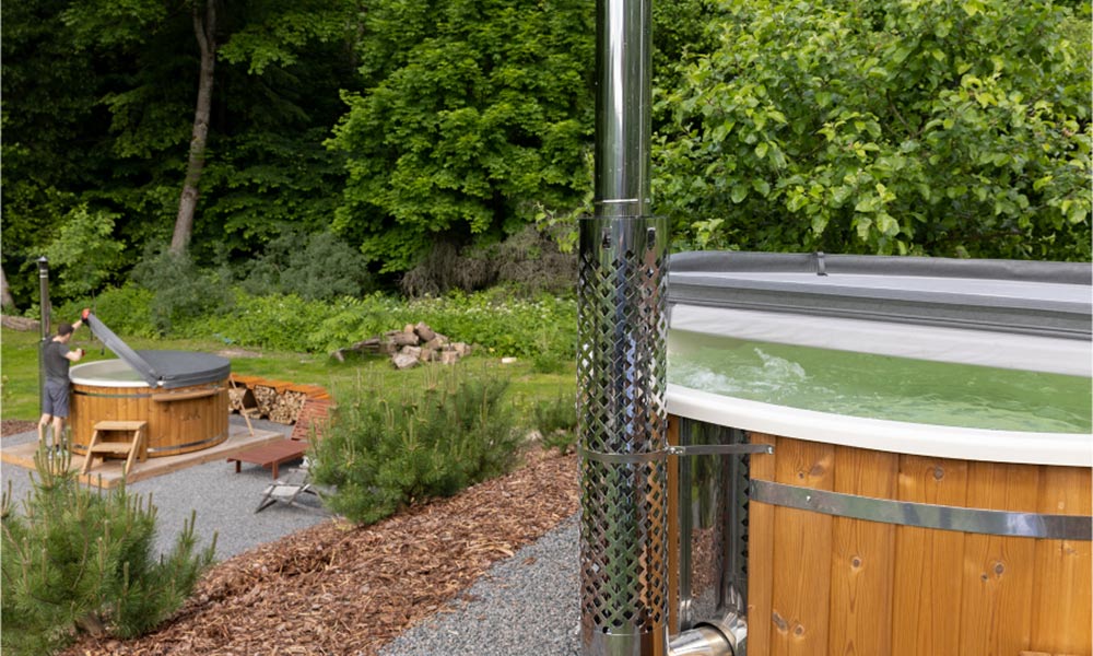 A garden with a hot tub in the distance, its lid open, and another hot tub closer by, with a white liner and bubbling water