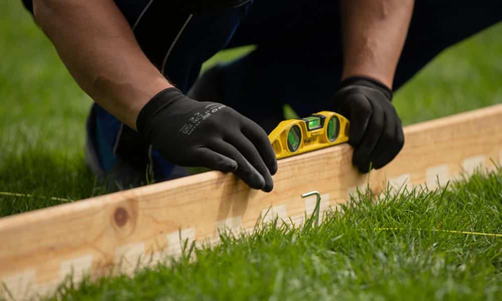 A person's hands measuring a wooden plank with a level