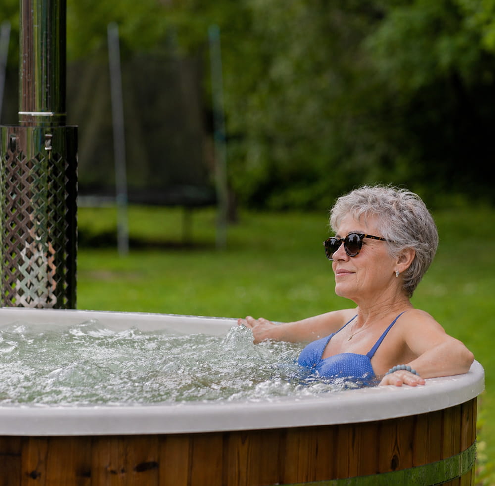 Woman in a hot tub outdoors with greenery in the background