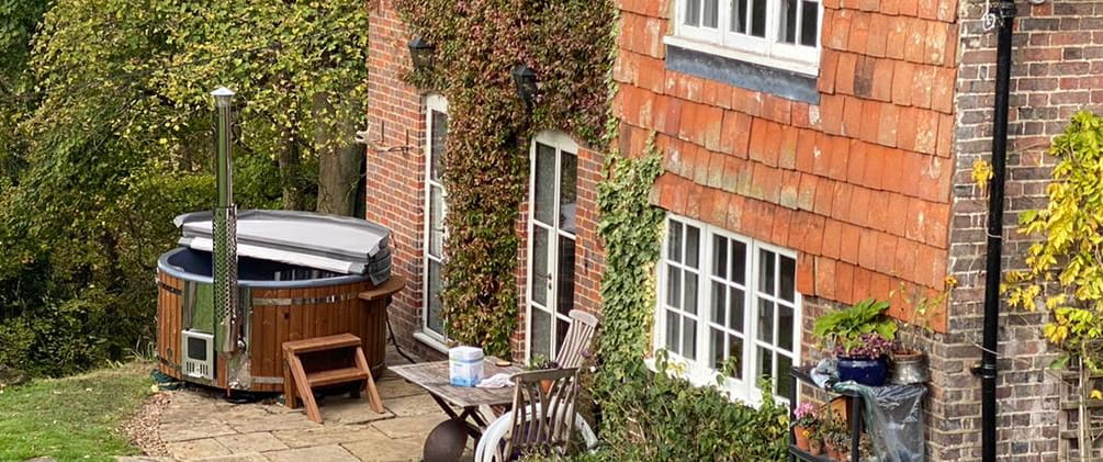 Wooden hot tub outside a red brick house with garden furniture.