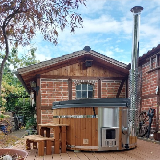 Runder Hot Tub im Außenbereich mit Edelstahlofen und Holztreppe auf einer Holzterrasse neben einem Backsteingebäude