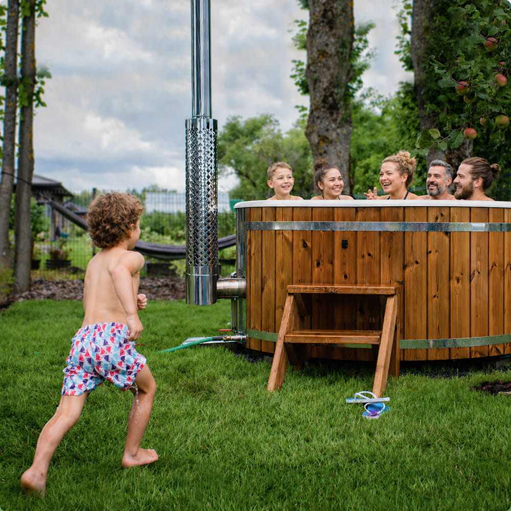 Family enjoying a hot tub in a garden with a child running towards it.