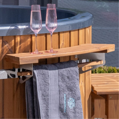 Nahaufnahme eines außenliegenden Holzregals, das an einem holzbefeuerten hot tub angebracht ist, mit Handtuchhalter und zwei Gläsern darauf.