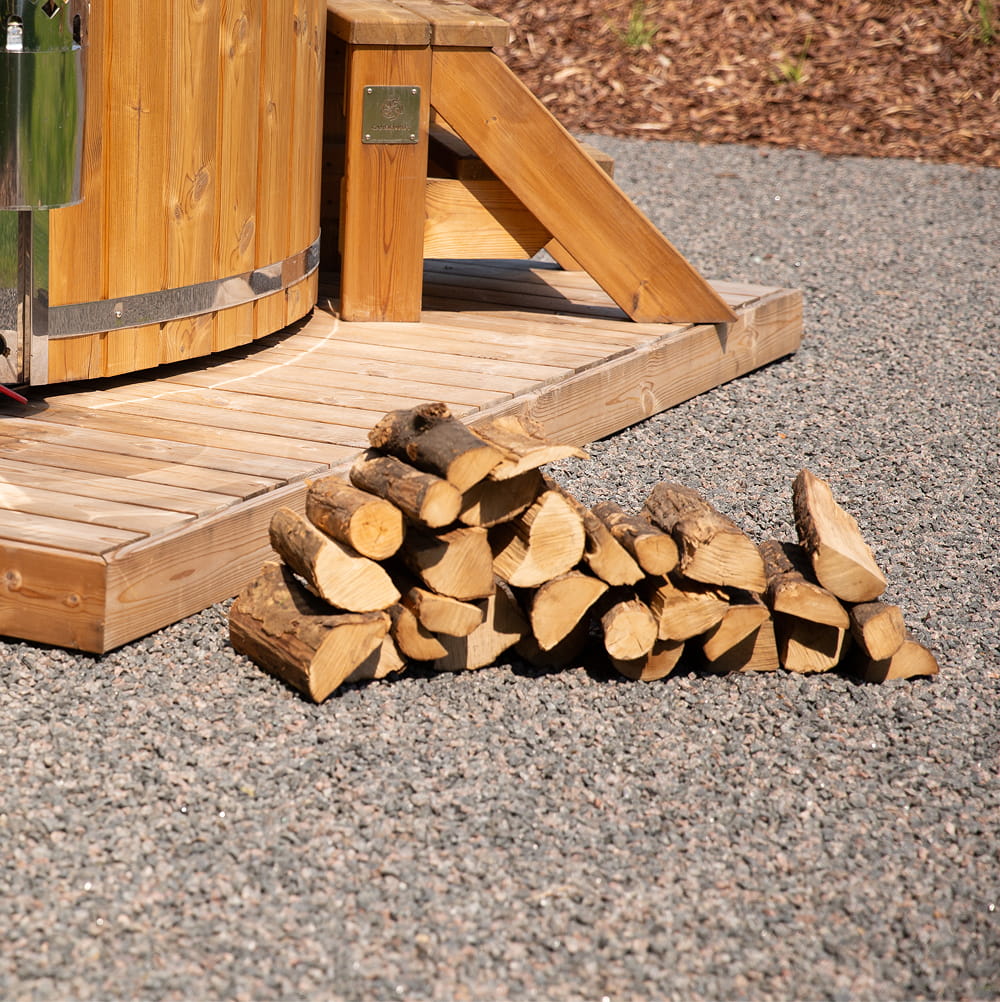 Stack of firewood in front of a wooden structure on a gravel surface