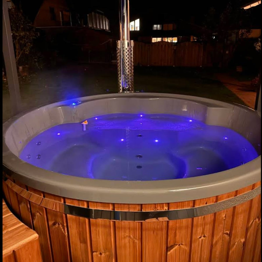 Nachtansicht eines beleuchteten, holzbefeuerten hot tub mit blauen LED-Leuchten und Edelstahlkamin im Außenbereich