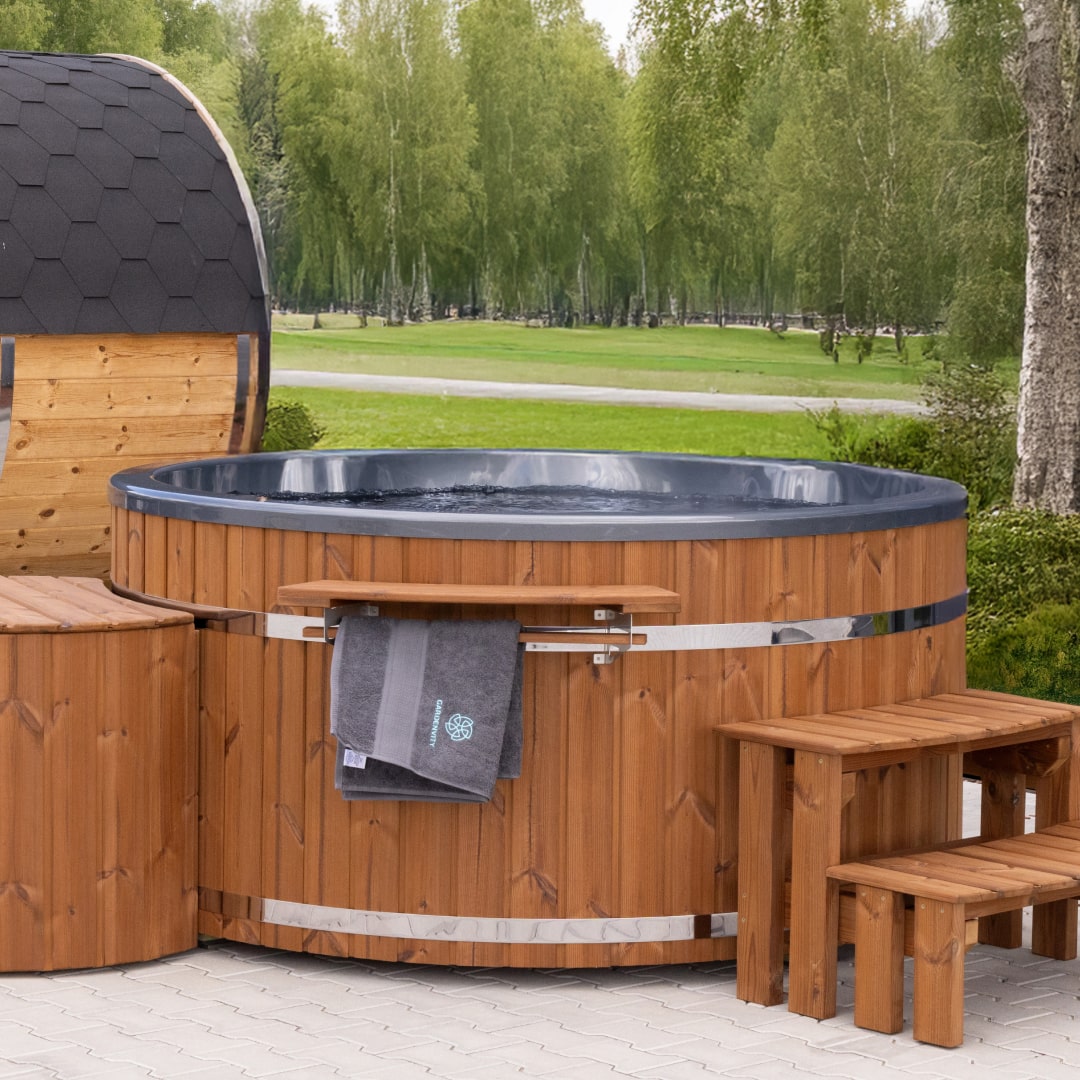 Außenansicht des holzbefeuerten Whirlpools mit dunklem Innenraum, Holzstufen, Handtuchhalter und einer nahegelegenen sechseckigen Saunakabine.