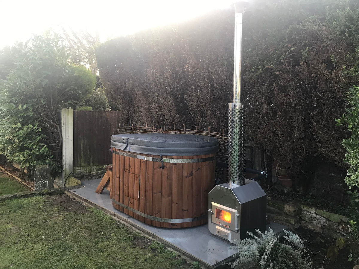 Außenansicht eines holzbefeuerten hot tub mit isolierter Abdeckung und Edelstahlofen in einer Gartenlandschaft