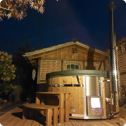 Wood-fired hot tub on a wooden deck at night with a house in the background